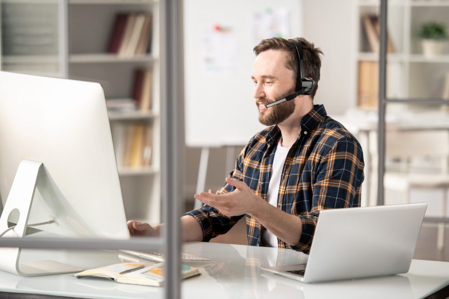 Confident operator explaining further details or answering question of client while sitting in front of computer screen